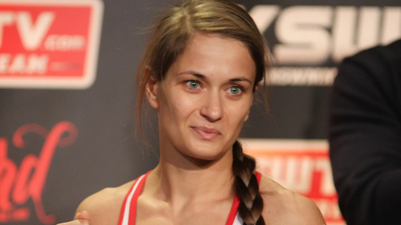 Karolina Kowalkiewicz z długim warkoczem, w białej koszulce sportowej, pozuje z zaciśniętymi pięściami podczas ważenia przed galą KSW